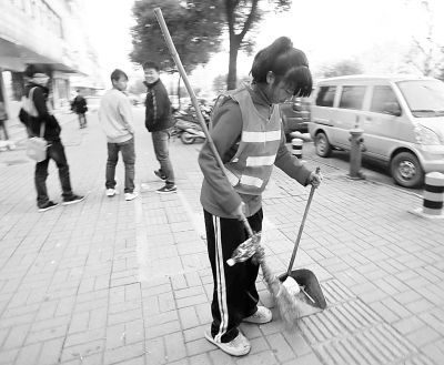   图为胡林家欣拿着比她人还高的扫帚在大街上扫地。记者李少文 摄 