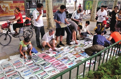 7月16日，市民们围聚在郑州街头的一个卖报摊前挑选报纸。